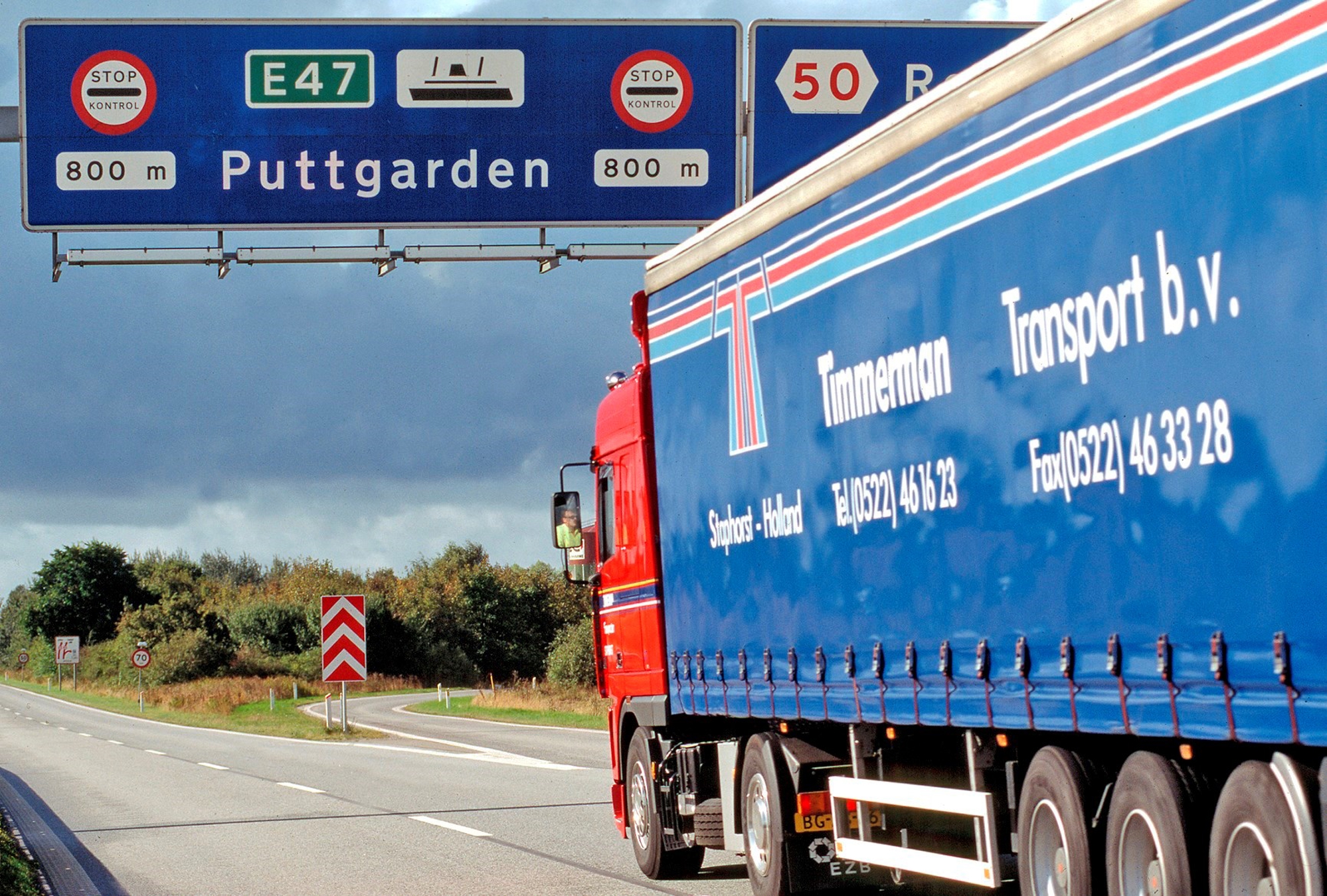 En blå lastbil kører under et motorvejsskilt hvorpå der står Puttgarden.
