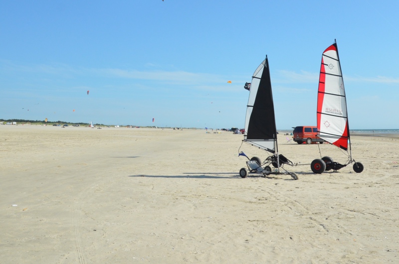 To strandsurfervogne parkeret på stranden i Fanø med drager i luften over stranden.