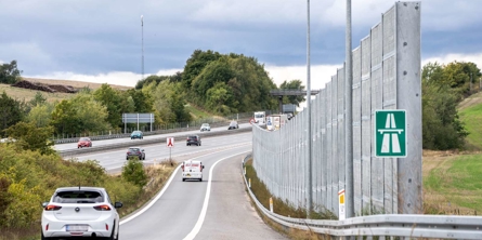 Støjskærm langs med en motorvejstilkørsel, hvor der kører et par biler