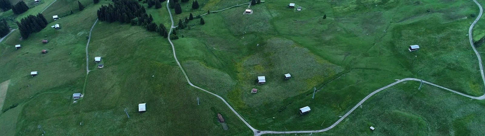 Luffoto af en grøn eng med spredte små huse og en vej, der snor sig igennem landskabet.